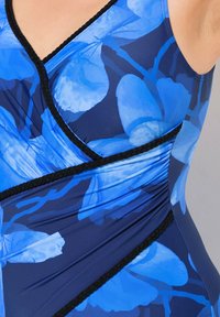 Maillot de bain floral bleu avec un design en couches et une bordure tressée noire. Le tissu a une texture lisse et extensible, augmentant le confort et l'ajustement.