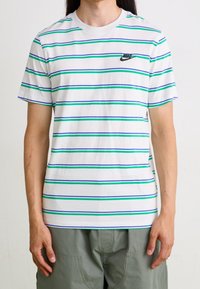 Bílý tričko s krátkým rukávem s horizontálními pruhy v zelené, modré a fialové barvě, s černým logem Nike na levé části hrudi.