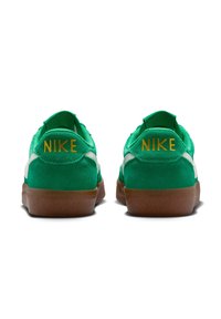 Zöld velúr tornacipő fehér részletekkel, barna gumitalppal és vörös "NIKE" felirattal a saroknál.