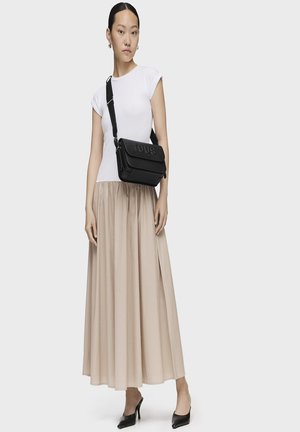 Bolso de cuero negro cruzado con logo "TOUS" en relieve, forma rectangular, correa ajustable, combinado con una camisa blanca y una falda beige.