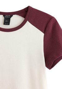 Kortärmad T-shirt med burgundy raglanärmar, kropp i vitt och rund halsringning. Tillverkad av mjukt bomullsblandat tyg.