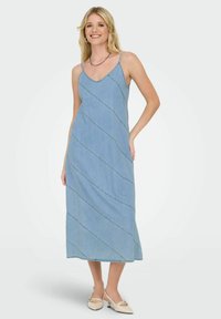 Ljusblå denim maxi-klänning med spaghetti-remsor, V-ringning och asymmetriska diagonala sömnadsmönster. Slät textur och avslappnad design.