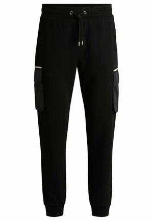 Jogging pants noirs en tissu doux avec taille à cordon, dotés de deux poches cargo, texture lisse et poignets côtelés aux chevilles.