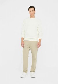 Maglione bianco a maglia, pantaloni beige e sneakers bianche. Outfit casual, con un design semplice, una texture morbida e una vestibilità comoda.