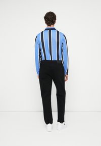 Koszula polo z długim rękawem, w niebiesko-granatowe paski, zestawiona z czarnymi spodniami i białymi sneakersami; gładki materiał z kołnierzykiem.