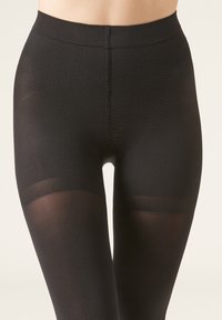Opaka svarta leggings tillverkade av elastiskt tyg, med ett strukturerat mönster vid midjan och en slät, genomskinlig finish på benen.