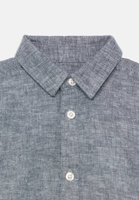 Pilka lino marškiniai su klasikiniais apykaklės, mygtukų eiliu su baltais mygtukais, tekstūruotu audiniu ir subtiliu audimo raštu.