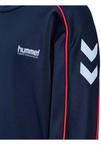 Marinblå sporttopp med röda detaljer, försedd med en vit logo och ett chevron-mönster på ärmen. Tillverkad av slät, syntetisk tyg.