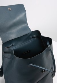 Ciemnozielona skórzana torba na ramię o gładkiej strukturze i metalowym zapięciu. Otwarta góra odsłania niepodszewkowane wnętrze z metką marki.