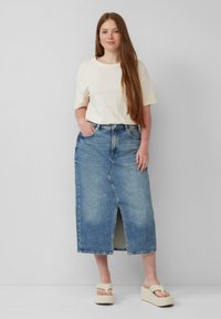 Jupe maxi en denim avec une fente à l'avant, délavage bleu clair et design classique. Associée à un t-shirt en crème doux et des sandales à plateforme.