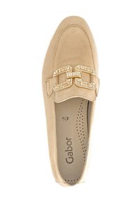 Beige Wildlederschuh mit flachem Design, ausgestattet mit einer dekorativen goldenen Schnalle und eingeprägtem Markenlogo im Inneren. Strukturierte Akzente entlang der Oberseite.