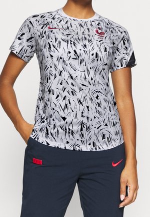 T-shirt de sport à manches courtes en gris clair avec un motif abstrait noir. Présente un logo Nike rouge et un col rond.