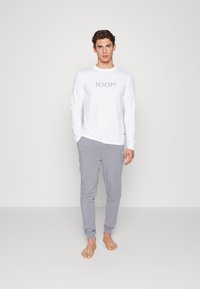 Hvit langermet skjorte med "JOOP!" i grå tekst, sammen med grå joggebukser. Begge plaggene har myk tekstur og en avslappet passform.