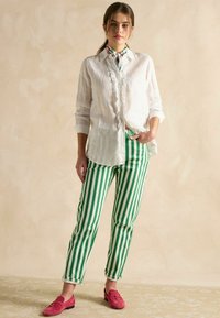 Biela ľanová košeľa s volánikovými detailmi, v kombinácii so zeleno-bielymi pruhovanými bavlnenými nohavicami. Rúžové zamšie mokasíny s kovovou ozdobou dokončujú outfit.