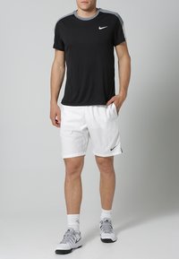 Sort kortærmet Nike t-shirt med grå detaljer, parret med hvide shorts og grå atletiske sko, der viser et afslappet sportswear-look.