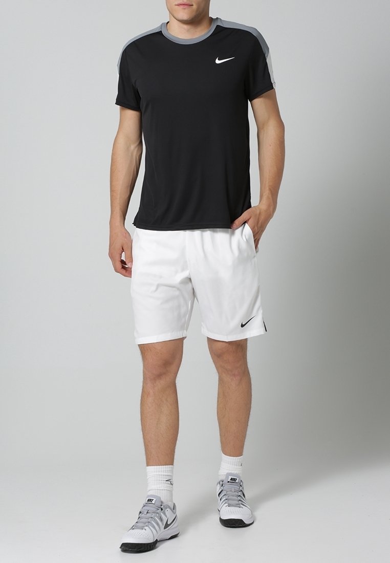 Sort kortærmet Nike t-shirt med grå detaljer, parret med hvide shorts og grå atletiske sko, der viser et afslappet sportswear-look.