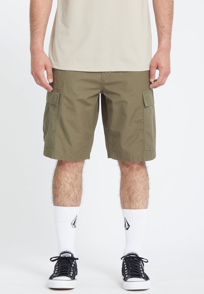 Olijfgroene cargoshorts met meerdere zakken, van katoen, tot op de knie en met een relaxte pasvorm, gecombineerd met zwarte sneakers en witte sokken.
