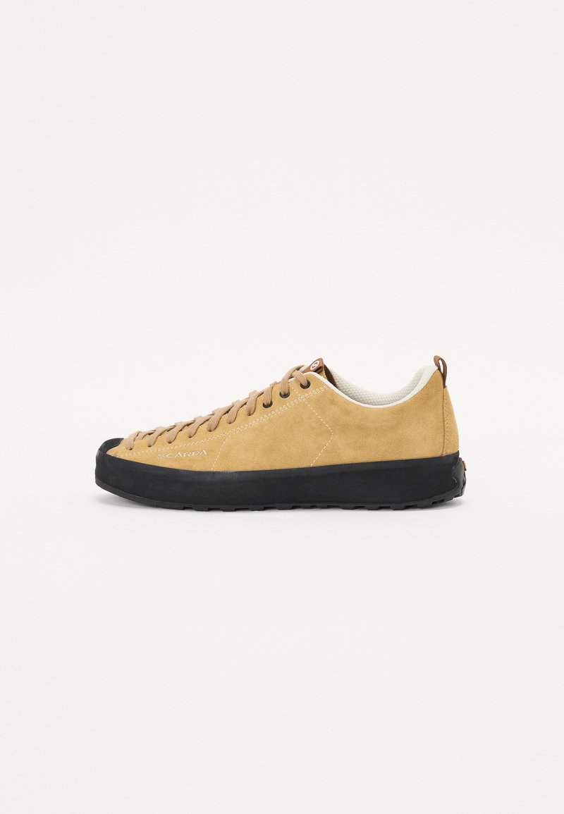 Tan suede sneaker with black rubber sole, rounded toe, and beige accent on the collar. Features brown laces and logo detail.