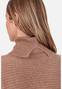 Pull côtelé marron clair avec un col montant et un détail texturé en forme d'empiècement sur le dos. Tissu doux avec une silhouette ajustée.