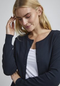 Mörkblå cardigan i strukturerad stickad kvalitet, med rund halsringning, långa ärmar och knäppning framtill.