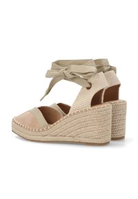 Sandalias de cuña de esparto en color beige con una parte superior de tela texturizada, cintas en el tobillo y plataforma de yute trenzado. Presenta detalles cosidos a lo largo de los bordes.