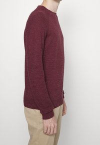 Bordeauxfarbener Rundhalsausschnitt-Pullover aus strukturiertem Strickstoff, mit gerippten Bündchen und Saum. Die Seitenansicht zeigt eine lässige Passform und ein schlichtes Design.