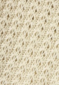 Stickad tyg, ljus krämfärgad, med ett mönster av texturerad spets som har öppna vävningar och mjuka, fluffiga fibrer.