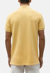 Camisa polo amarilla de manga corta, con cuello tipo solapa y dobladillo recto. Textura suave y corte ajustado.