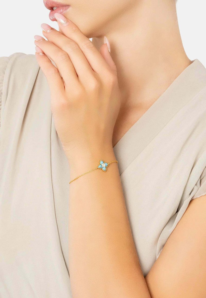 Guldkedjearmband med ett blommönster som har tre turkosa stenar. Slät yta, delikat och minimalisk stil.