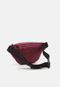Burgundy quilted nylon fanny pack with a curved shape, adjustable black strap, zippered closure, and diamond pattern on the surface.
