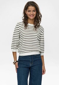 Vit- och brunspräcklig tröja med trekvartsärmar, ribbad textur och scalloped nederkant, matchad med blå utsvängda jeans.