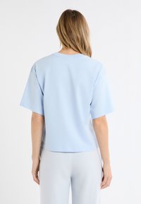 Jasnoniebieska koszulka na krótki rękaw o luźnym kroju i okrągłym dekolcie. Gładka tekstura i prosty design, noszona z jasnoniebieskimi, kraciastymi spodniami.