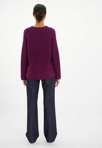 Pull en tricot violet avec un motif texturé, ourlet côtelé et manches longues, associé à un jean évasé bleu foncé. Vue de dos.