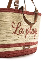 Bolso de paja tejido en beige y rojo con "La plage" bordado en rojo, asas de cuero marrón y una etiqueta de la marca en el lateral.