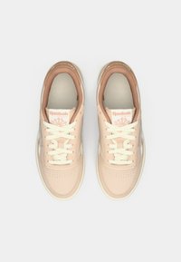 Un paio di sneakers Reebok Classic beige con lacci bianchi, viste dall'alto su uno sfondo bianco.