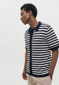 Adīts īsām piedurknēm polo krekls jūras zila un krēmkrāsas svītrās. Iespējas ar pogājamu priekšpusi un kontrastējošu apkakli. Tekstūrēta auduma.