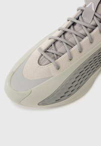 Scarpa sportiva grigia chiara con tomaia in rete, accenti testurizzati, sovrapposizioni beige e una suola distintiva a motivo esagonale.