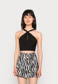 Top halter cropped preto com detalhe em nó, combinado com uma saia mini de cintura alta com um padrão de estampa de zebra em preto e branco.