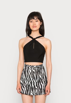 Top halter cropped preto com detalhe em nó, combinado com uma saia mini de cintura alta com um padrão de estampa de zebra em preto e branco.