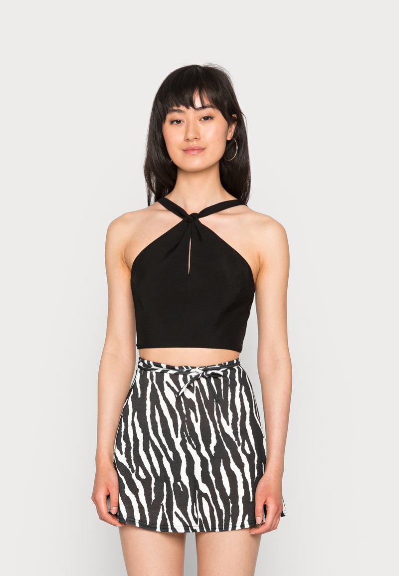 Top halter cropped preto com detalhe em nó, combinado com uma saia mini de cintura alta com um padrão de estampa de zebra em preto e branco.