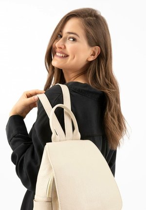 Sac à dos en cuir beige avec une surface texturée, doté d'une fermeture éclair, d'une forme arrondie et de bretelles doubles pour un port facile.