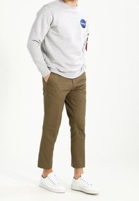 Sudadera gris con el logo de la NASA, pantalones slim-fit beige y zapatillas blancas. Tela suave, diseño casual, con cuello redondo y costuras visibles.