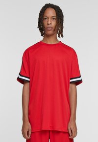 Tricou sportiv roșu cu mâneci scurte, având dungi de accent alb-negru pe mâneci și un guler rotund. Textură netedă.