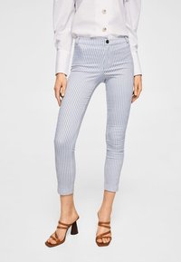 Modré a bílé pruhované skinny kalhoty s vysokým pasem, s předním zapínáním na knoflík a hladkou strukturou. V kombinaci s hnědými sandály na podpatku.