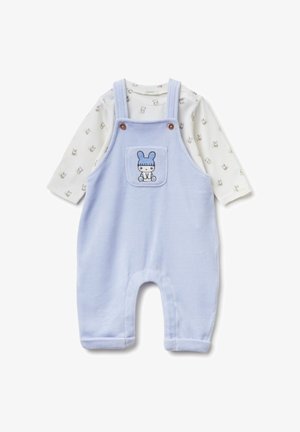 Salopette azzurra in tessuto morbido con una tasca frontale decorata con un ricamo di coniglio. Sotto si intravede una camicia bianca a maniche lunghe con stampa di conigli.