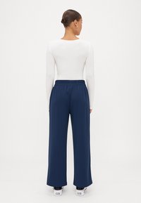 Meripanjang navy dengan waistband elastis, dipadukan dengan atasan putih lengan panjang. Tekstur halus, gaya kasual, dipakai dengan sneakers putih.