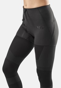 Black compression leggings with a high waistband, featuring textured panels, drawstring closure, and a logo on the side.