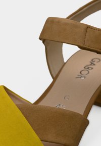 Σανδάλια Gabor με λουράκι από σουέτ σε κίτρινο χρώμα στο μπροστινό μέρος και λουράκι στον αστράγαλο σε ταμπά σουέτ. Λεία εσωτερική επιφάνεια με ανάγλυφο λογότυπο της μάρκας.