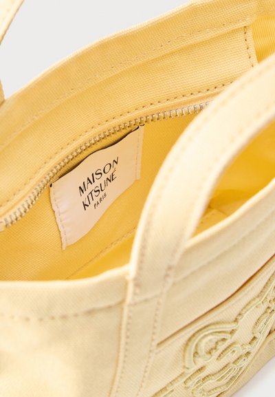 Sac fourre-tout en toile jaune avec poche zippée à l'intérieur, doté d'une étiquette Maison Kitsuné Paris et d'un logo brodé sur l'extérieur.