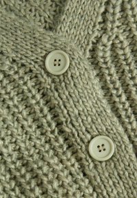 Gehaakte cardigan van zachte, lichtgroene wol met een gestructureerd patroon. Bevat twee crèmekleurige knopen met elk vier gaten voor het sluiten.